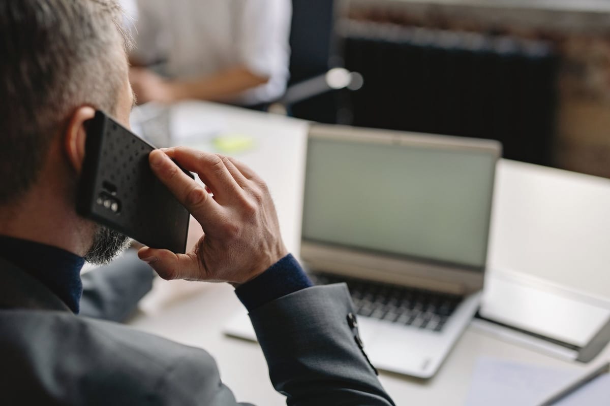 Professional man using cellphone in office setting, multitasking with a laptop.